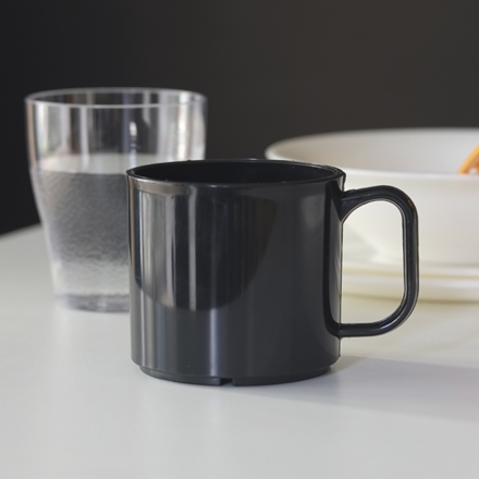 A black unbreakable coffe mug with an ear and tableware in the background